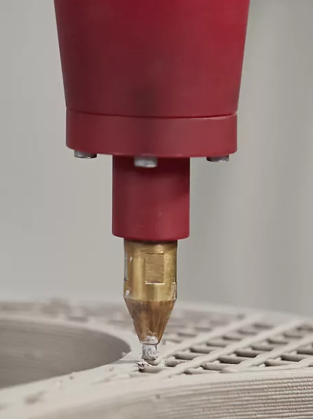 Close-up detail of a Rock.01 sink being 3D printed. The print nozzle is applying the vitreous china material to a partially completed sink, showing the internal bracing structure and the exterior layers from the printing process.
